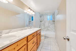 Full bathroom featuring tiled shower / bath combo, dual bowl vanity, toilet, and tile flooring