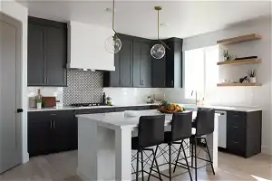 Kitchen with decorative light fixtures, light hardwood / wood-style flooring, backsplash, and a kitchen island