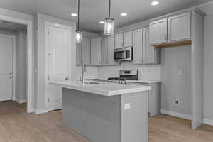 Kitchen featuring decorative light fixtures, appliances with stainless steel finishes, a center island with sink, light hardwood / wood-style floors, and tasteful backsplash