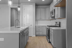 Kitchen featuring appliances with stainless steel finishes, sink, light hardwood / wood-style floors, gray cabinets, and a kitchen island with sink