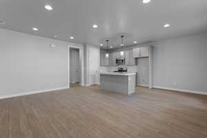 Kitchen with pendant lighting, light wood-type flooring, a kitchen island with sink, and stove