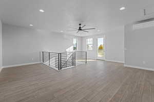 Spare room featuring a wall unit AC, light hardwood / wood-style floors, and ceiling fan