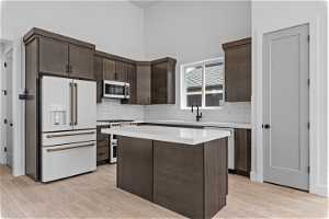 Kitchen featuring a center island, light hardwood / wood-style floors, appliances with stainless steel finishes, backsplash, and dark brown cabinetry