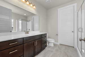 Bathroom with a shower with door, toilet, tile flooring, and large vanity