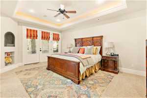 Bedroom featuring ceiling fan, carpet flooring, access to exterior, and a tray ceiling