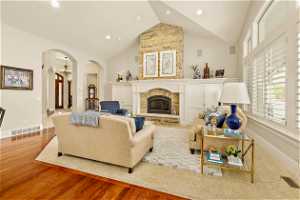 Living room featuring a stone fireplace, a notable chandelier, high vaulted ceiling, and hardwood / wood-style floors