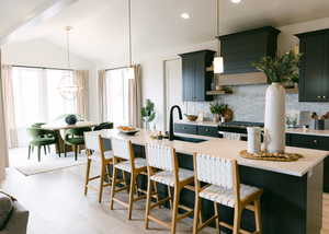 Kitchen with lofted ceiling, decorative backsplash, sink, hanging light fixtures, and an island with sink