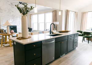 Kitchen featuring dishwasher, pendant lighting, a center island with sink, sink, and light wood-type flooring