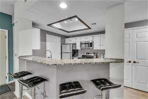 Kitchen with white cabinets, light hardwood / wood-style floors, a kitchen breakfast bar, and stainless steel appliances