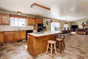 Kitchen featuring sink, a center island with sink, light tile floors, and black appliances