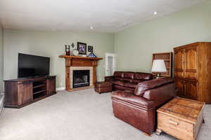 Living room with a tiled fireplace, light carpet, and lofted ceiling