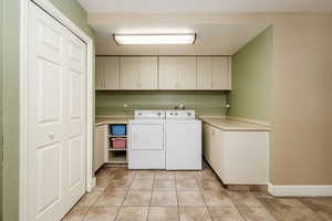 Laundry room with cabinets, separate washer and dryer, and light tile floors