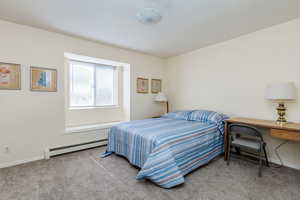 Bedroom with a baseboard heating unit and carpet floors