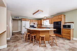 Kitchen with a center island, black appliances, a kitchen bar, and light tile flooring