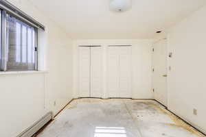 Unfurnished bedroom featuring multiple closets and a baseboard radiator