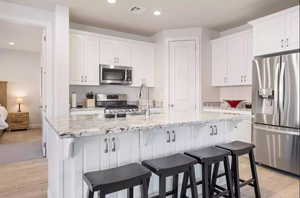 Kitchen with white cabinets, a center island with sink, light hardwood / wood-style floors, and stainless steel appliances