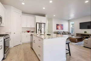 Kitchen with a breakfast bar area, stainless steel appliances, light wood-type flooring, and a center island with sink