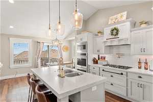 Kitchen featuring backsplash, lofted ceiling, stainless steel appliances, and white cabinetry