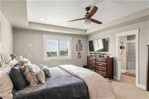 Bedroom featuring light hardwood / wood-style flooring, a raised ceiling, ceiling fan, and ensuite bathroom