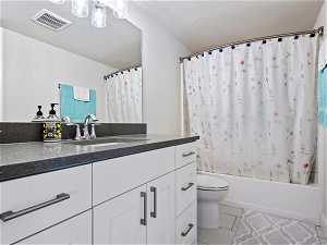 Full bathroom with shower / tub combo, toilet, a textured ceiling, vanity, and tile floors