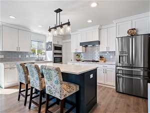 Kitchen with a kitchen island, wall chimney range hood, backsplash, stainless steel appliances, and wood-type flooring