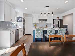 Kitchen featuring backsplash, light hardwood / wood-style flooring, stainless steel appliances, and hanging light fixtures
