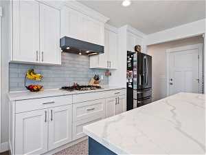 Kitchen featuring tasteful backsplash, wall chimney range hood, stainless steel appliances, and white cabinetry
