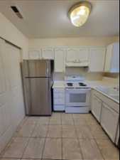 Kitchen with white cabinetry, white range with electric stovetop, stainless steel fridge, and light tile flooring