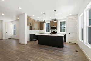 Kitchen with hanging light fixtures, an island with sink, tasteful backsplash, and wood-type flooring