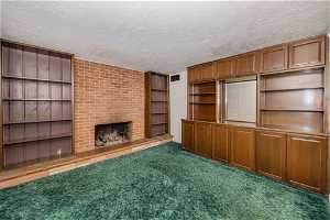 Unfurnished living room with a textured ceiling, dark colored carpet, brick wall, and a brick fireplace