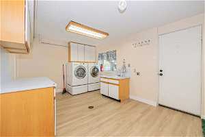 Laundry area featuring washer and clothes dryer, light hardwood / wood-style flooring, cabinets, and sink