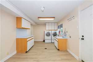 Kitchen featuring white cabinets, washing machine and dryer, light wood-type flooring, and a textured ceiling