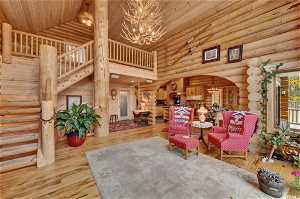 Living room with log walls, high vaulted ceiling, a notable chandelier, wooden ceiling, and light hardwood / wood-style flooring
