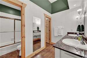 Full bathroom with hardwood / wood-style flooring, toilet, bath / shower combo with glass door, and double sink vanity