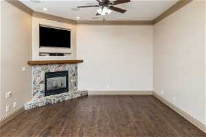Unfurnished living room with ceiling fan, crown molding, a stone fireplace, and dark wood-type flooring