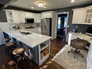 Kitchen with appliances with stainless steel finishes, dark wood flooring, kitchen peninsula, and white cabinets