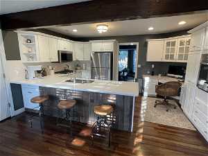 Kitchen featuring dark hardwood / wood-style flooring, white cabinetry, kitchen peninsula, appliances with stainless steel finishes, and a kitchen bar