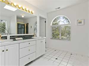 Primary bathroom featuring a skylight, double vanity, and tile flooring