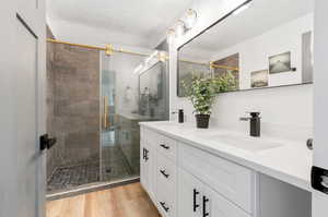 Ensuite bathroom with a shower with door, LVP wood-type flooring, oversized vanity, and double sink