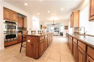 Kitchen featuring a center island, backsplash, stainless steel appliances, granite countertops, double ovens, gas range, large pantry, and a kitchen breakfast bar