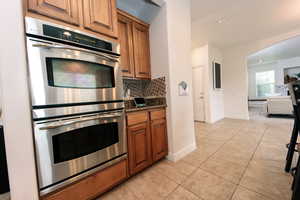 Kitchen with stainless steel double oven, dark stone countertops, tasteful backsplash, and light tile flooring