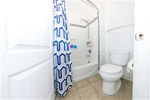 Main bathroom with tile floors, toilet, and shower / bath combo with shower curtain