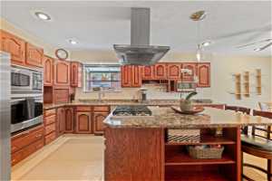 Kitchen with appliances with stainless steel finishes, backsplash, island exhaust hood, sink, and a center island