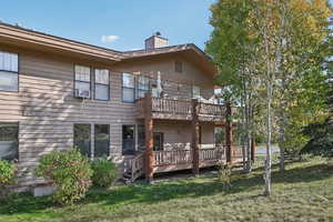 Rear view of property with a deck, cooling unit, and a lawn