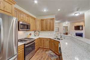 Kitchen with light stone counters, a fireplace, sink, stainless steel appliances, and light hardwood / wood-style flooring