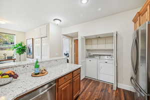 Kitchen featuring dark wood-type flooring, light stone countertops, washer and dryer, and appliances with stainless steel finishes