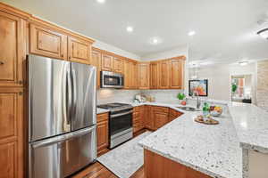 Kitchen with light stone counters, sink, kitchen peninsula, stainless steel appliances, and light hardwood / wood-style floors