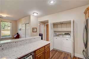 Kitchen featuring light stone countertops, dark hardwood / wood-style flooring, stainless steel fridge, and washer and dryer