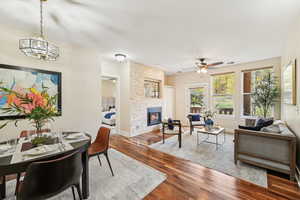 Dining space featuring dark wood-type flooring, ceiling fan with notable chandelier, and a stone fireplace