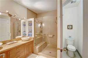 Bathroom featuring vanity with extensive cabinet space, an enclosed shower, toilet, and tile flooring